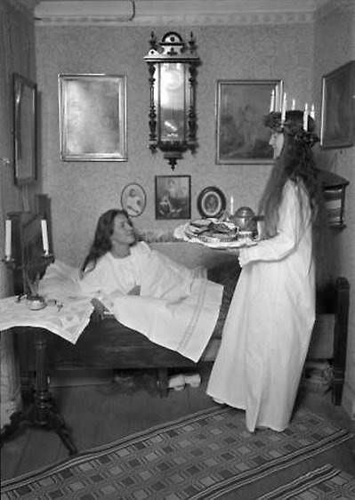svartvitt fotografi med vitklädd lucia som uppvaktar kvinna i säng med kaffebricka